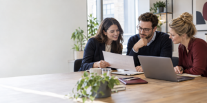 Three colleagues planning a client onboarding process with a laptop and printed workflow